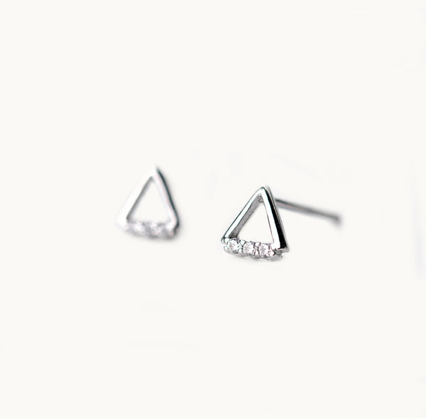 Une paire de boucles d'oreilles est exposée devant un fond beige.  Ce sont des triangles en argent 925 avec trois strass sur le bas. 