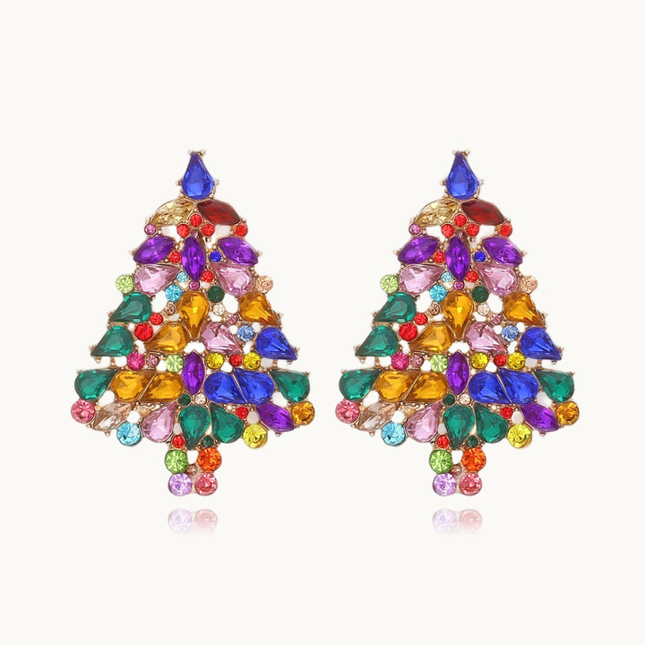 Une paire de boucles d'oreille est exposée devant un fond beige.  Ce sont des boucles d'oreille en forme de sapin tout en strass et pierres multicolores. 