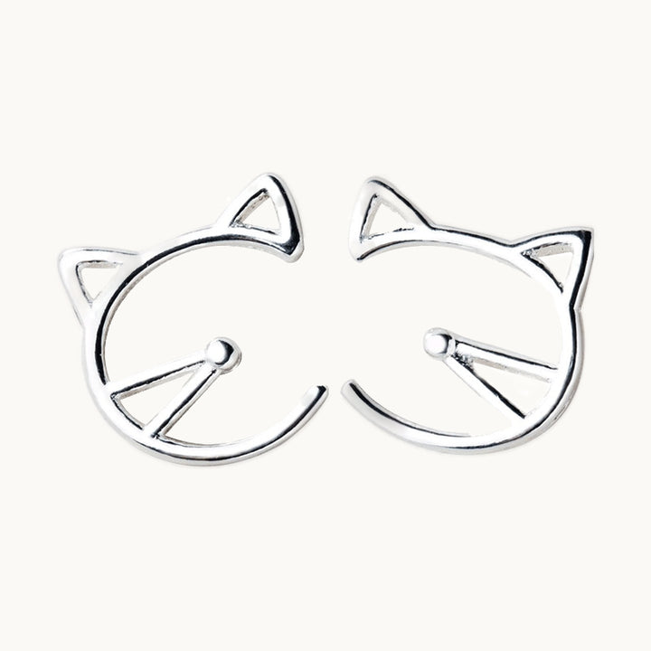Une paire de boucles d'oreilles est exposée devant un fond beige.  Ce sont des boucles rondes en forme de tête de chat. Elles sont en argent 925. 
