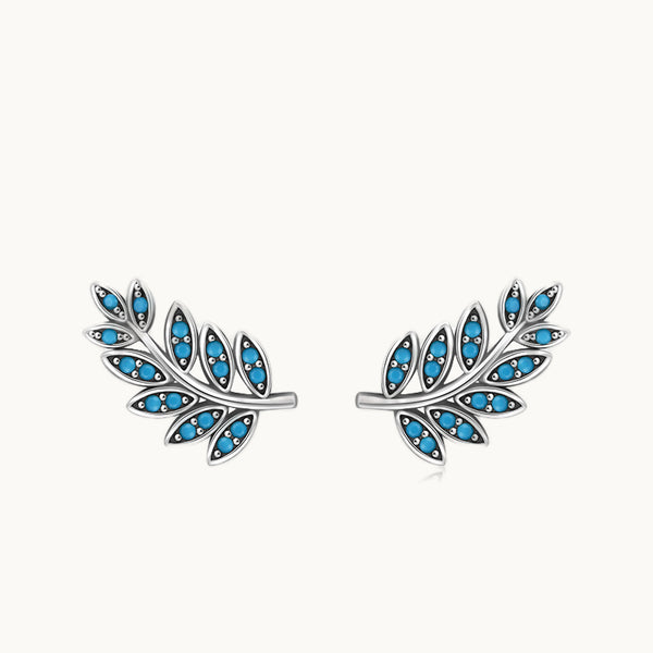 Une paire de boucles d'oreilles est exposée devant un fond beige.  Ce sont des boucles d'oreille grimpantes en forme de feuilles.  Elles sont en argent 925 et sont ornées de pierres turquoises.