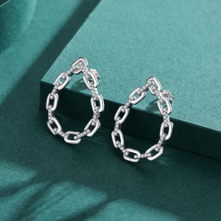 Une paire de boucles d'oreille pendantes en argent 925 avec des maillons de chaîne et des strass étincelants. Un design unique en forme de goutte qui sublime votre allure. Idéales pour les occasions spéciales ou pour ajouter une touche d'élégance au quotidien. Poids : 4,58 g. Dimensions : 27 x 21 mm.