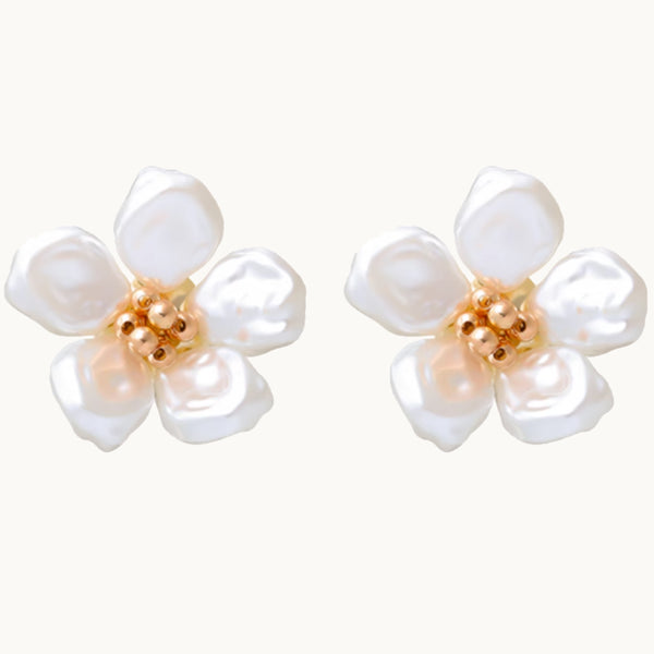 Une paire de boucles d'oreilles est exposée devant un fond beige.  Ce sont des fleurs avec un coeur doré et des pétales en perles. 