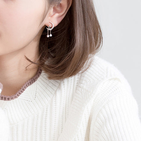 Une femme porte des boucles d'oreille en forme de lune avec une étoile et des diamants pendants. Un design délicat qui évoque un ciel étoilé. Parfait pour une élégance intemporelle et moderne.