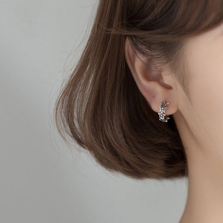 Boucle d'oreille créole étoiles argent vieilli - Femme - Argent 925. Une vue rapprochée de l'oreille d'une femme portant des boucles d'oreille créoles en forme d'étoiles, ajoutant une touche vintage et originale à sa parure.