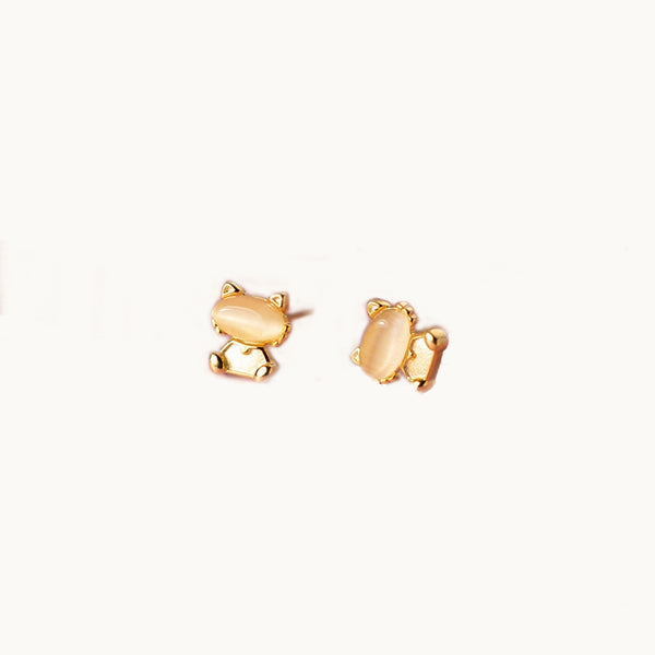 Une paire de boucles d'oreilles est exposée devant un fond beige.  Ce sont des boucles d'oreille chat. La tête du chat est une pierre de style opale. . 