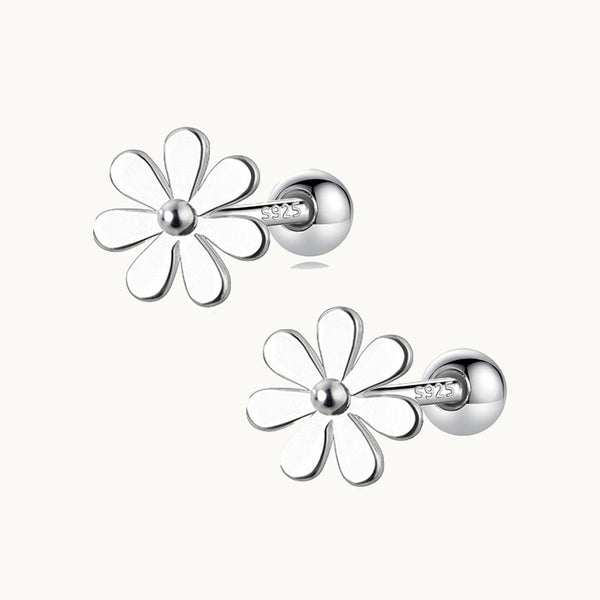 Une paire de boucles d'oreilles est exposée devant un fond beige.  Ce sont des fleurs blanches en argent. 