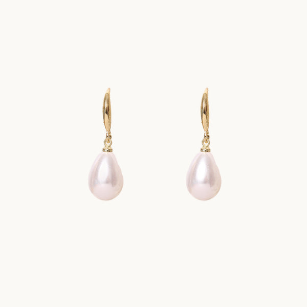 Une paire de boucles d'oreilles est exposée devant un fond beige.  Elles sont pendantes avec une tige dorée et une perle ovale. 