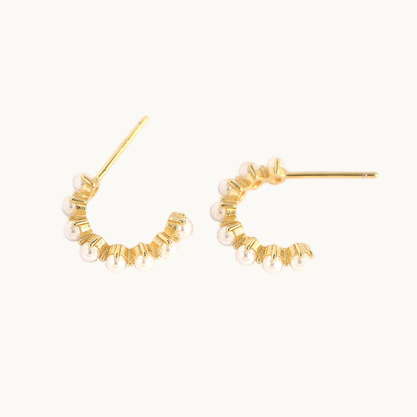 Une paire de boucles d'oreilles est exposée devant un fond beige.  Ce sont des créoles ornées de petites perles tout du long. Elles sont en argent 925 plaqué or.