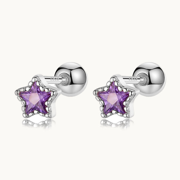 Une paire de boucles d'oreilles est exposée devant un fond beige.  Ce sont des étoiles en strass violettes. Les boucles sont en argent