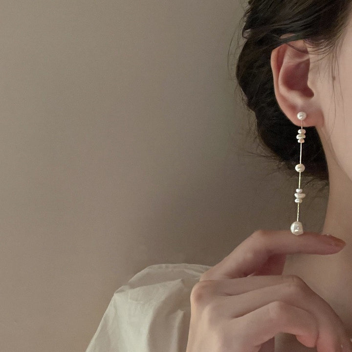 Une femme porte une boucle d'oreille en perle d'eau douce, pendante sur une chaîne en or. Un choix élégant pour toutes occasions.