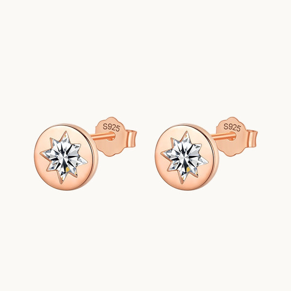 Une paire de boucles d'oreilles est exposée devant un fond beige.  Ce sont des boucles d'oreille rondes avec une étoile en diamant au milieu. Elles existent en argent 925 plaqué or rose. 