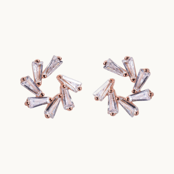 Une paire de boucles d'oreilles est exposée devant un fond beige.  Ce sont des boucles d'oreilles rondes. Elles sont ornées de petits diamants rectangulaires qui forment un soleil. Elles sont en argent 925 plaqué or rose.