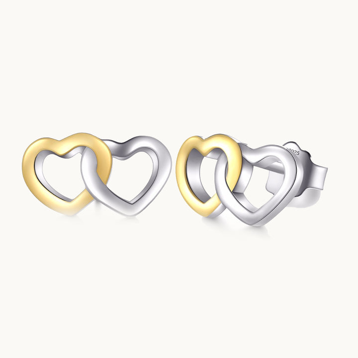 Une paire de boucles d'oreilles est exposée devant un fond beige.  Ce sont des boucles d'oreilles double coeur. l'un est en argent 925 et l'autre en argent 925 plaqué or. 