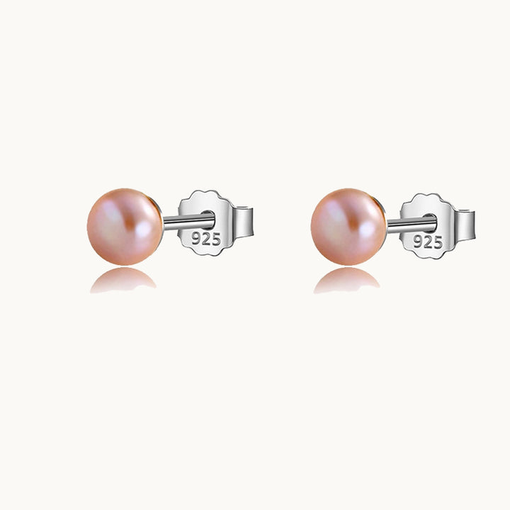 Une paire de boucles d'oreilles est exposée devant un fond beige.  Ces boucles sont de petites perles. Les perles sont roses et les boucles sont en argent 925.
