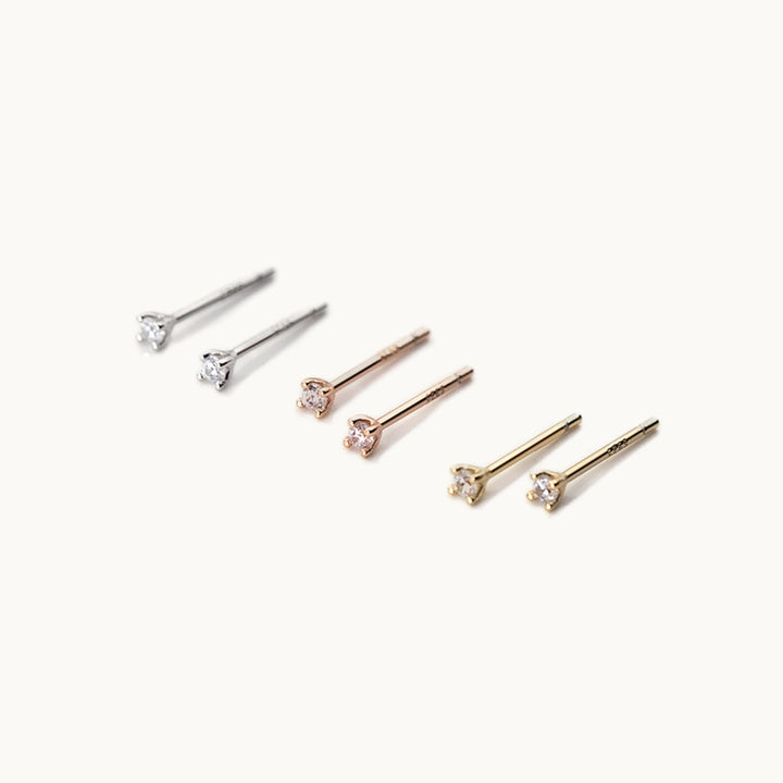 Trois paires de boucles d'oreille sont exposées sur un fond beige. Ce sont de tous petits diamants. Il y a une paire en argent, une en plaqué or et une en plaqué or rose. 