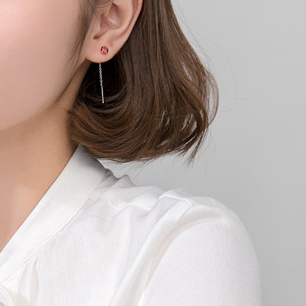 Une femme porte une boucle d'oreille pendante en argent 925 avec un diamant éclatant à l'extrémité de la chaîne. Un accessoire raffiné et contemporain pour toutes occasions.