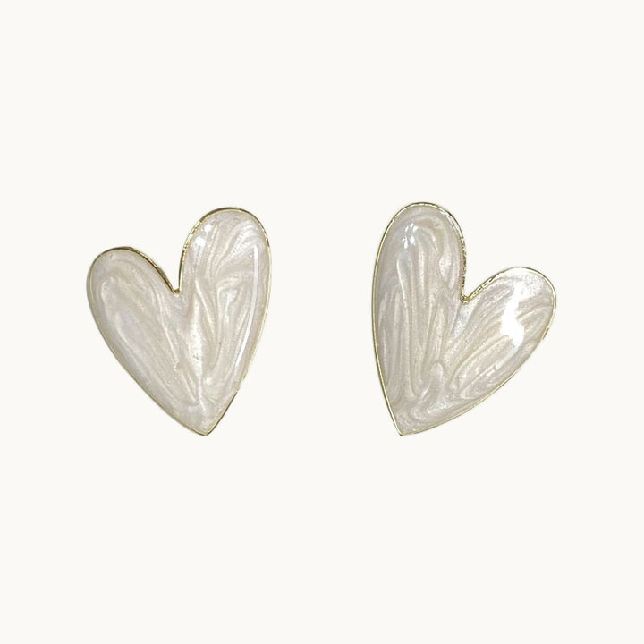 Une paire de boucles d'oreilles est exposée devant un fond beige.  Ce sont des coeurs géants marbrés blancs. 