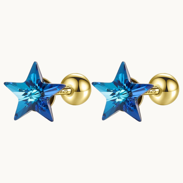 Une paire de boucles d'oreilles est exposée devant un fond beige.  Ce sont des étoiles bleues et les boucles sont en or. 