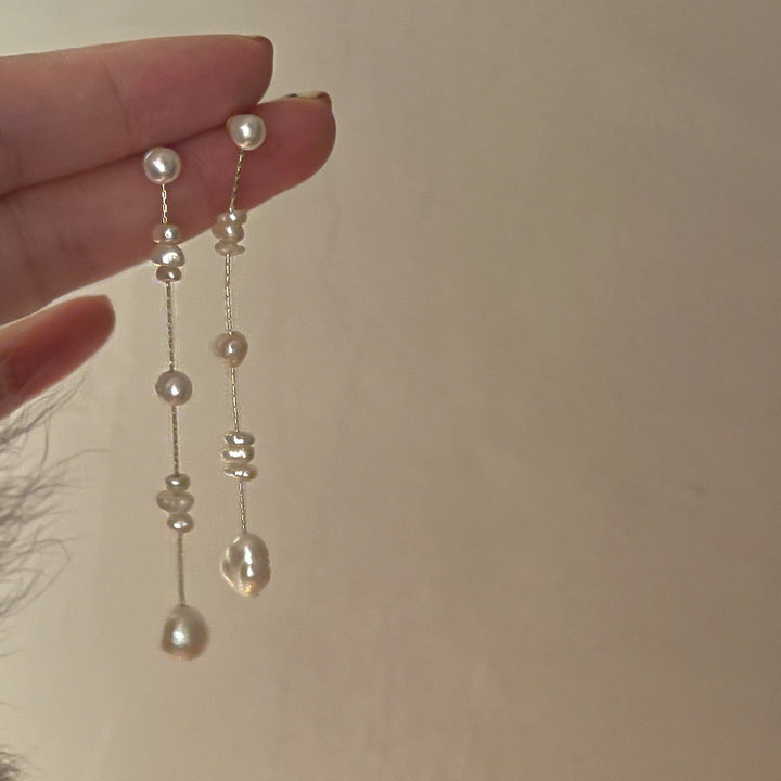 Une personne tenant une paire de boucles d'oreille longues et pendantes avec des perles d'eau douce. Un choix élégant pour toutes occasions.