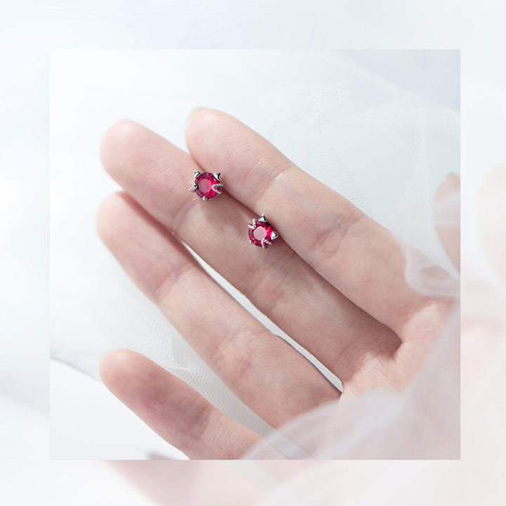 Une main tenant une paire de boucles d'oreilles en forme de chat avec une tête scintillante en diamant de zirconium couleur rouge rubis. Matériau : Argent 925, Argent 925 plaqué or rose. Dimensions : 0,7 x 0,7 cm. Style : Boucle d'oreille diamant, rubis, rouge.