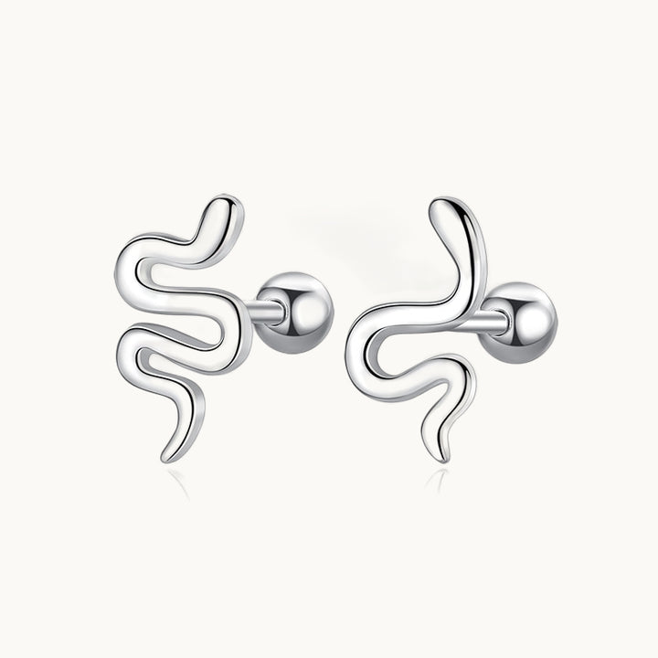 Une paire de boucles d'oreilles est exposée devant un fond beige.  Ce sont des serpents en argent. 