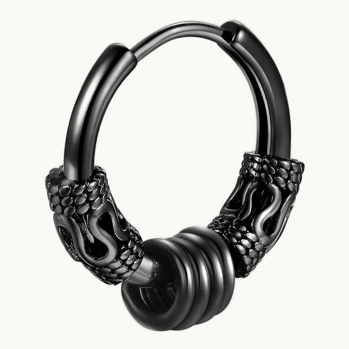 Une boucle d'oreille est exposée devant un fond beige.  C'est une petite créole noire ornée de bagues larges avec des motifs serpent. Entre les deux bagues il y a une multitude de petites anneaux qui entourent la créole.