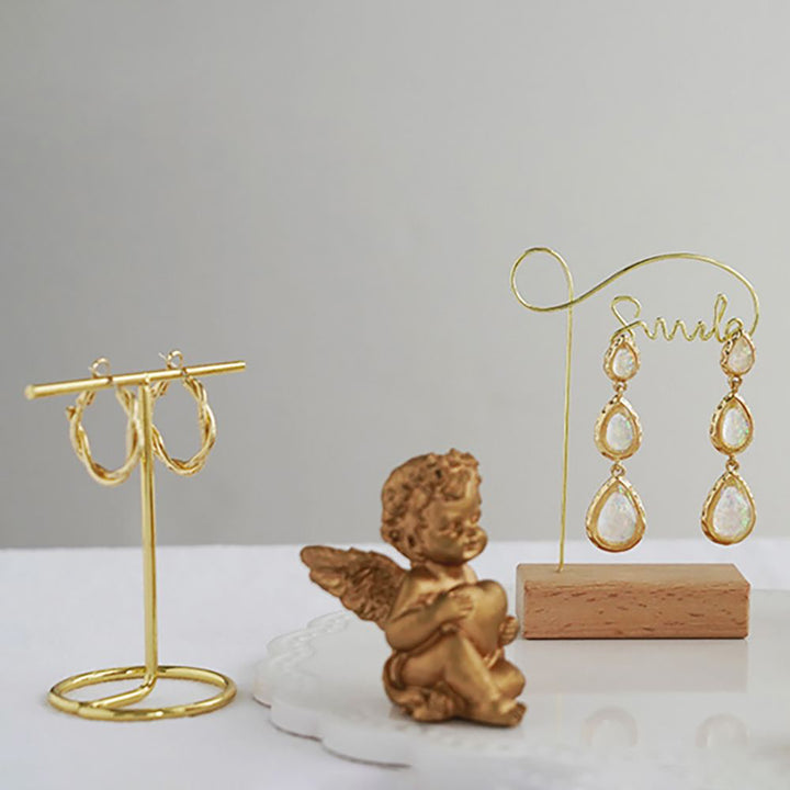 Un présentoir en bois et métal doré pour boucles d'oreille, avec des formes variées : U inversé, angle droit, "smile" et métallique en T. Élégant et contemporain.
