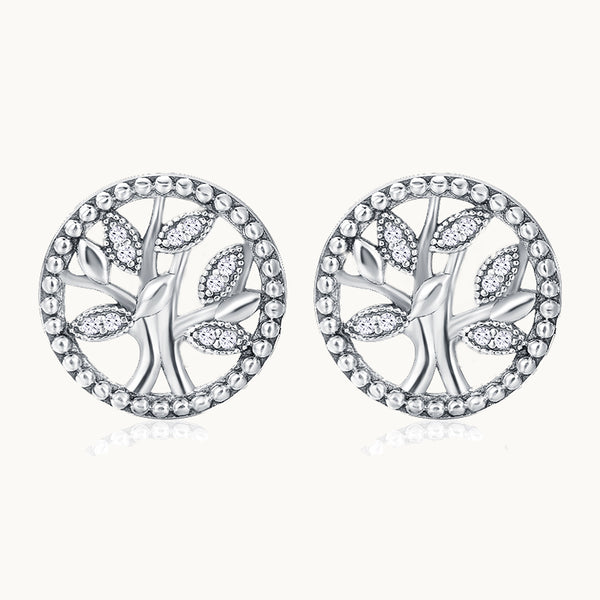 Une paire de boucles d'oreilles est exposée devant un fond beige.  Ce sont des boucles rondes en forme d'arbre de vie orné de strass. Elles sont en argent 925. 