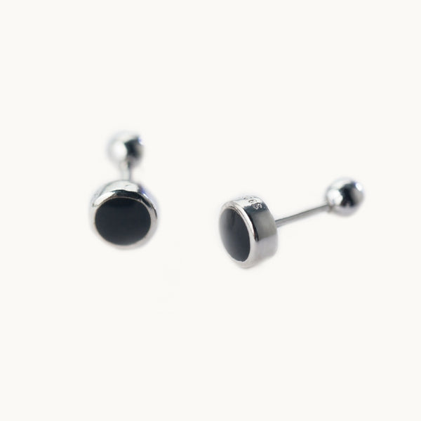 Une paire de boucles d'oreilles est exposée devant un fond beige.  Ce sont des boucles d'oreilles rondes.  Elles sont en argent 925 avec un rond noir au milieu. La tige est droite et la fermeture est sécurisée à l'arrière par une boule pour ne pas se ferme mal ou ne pas perdre la boucle.