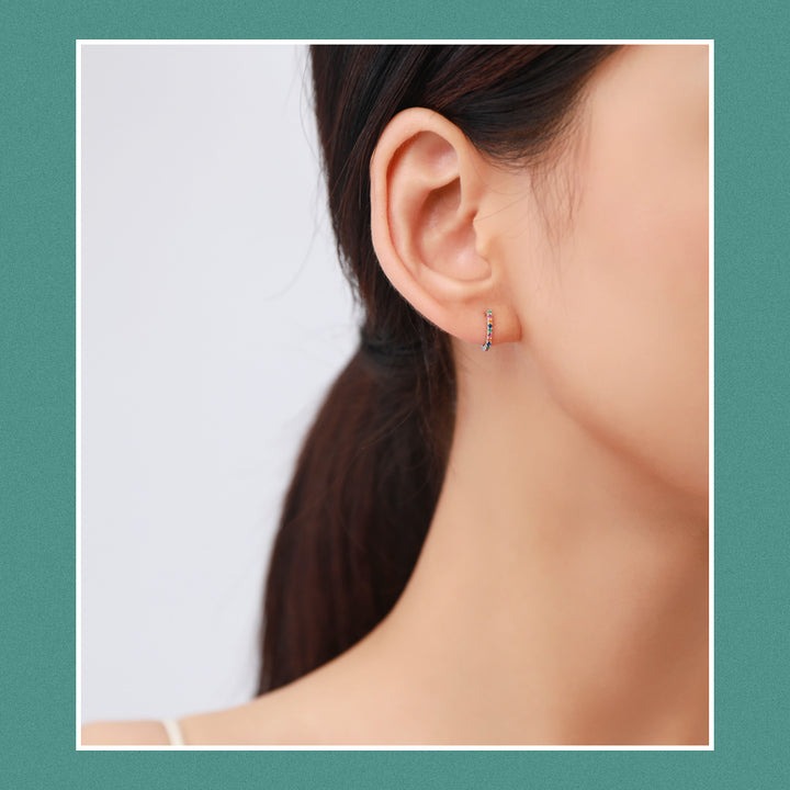 Une oreille de femme de près avec une boucle d'oreille demi anneau strass colorés en argent 925. Élégance discrète et design intemporel.