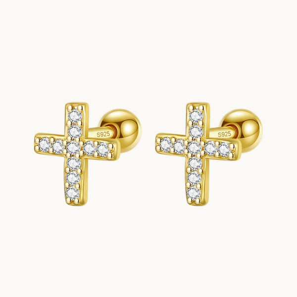  Une paire de boucles d'oreilles est exposée devant un fond beige.  Ce sont des boucles d'oreille croix en strass. Les boucles sont dorées. 