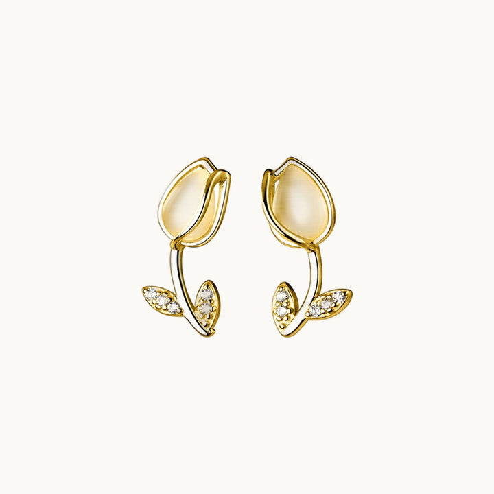 Une paire de boucles d'oreilles est exposée devant un fond beige.  Ce sont des tulipes avec une pierre opale dans le buble et des strass sur les feuilles. Elles sont en argent 925 plaqué or.