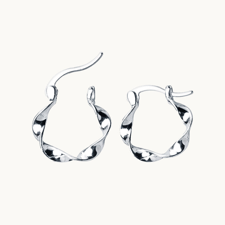 Une paire de boucles d'oreilles est exposée devant un fond beige.  Ce sont des créoles torsadées. Elles sont en argent 925. 