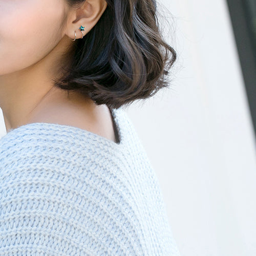 Une femme portant un pull blanc et des boucles d'oreille spirales grimpantes avec une étoile bleue en strass.