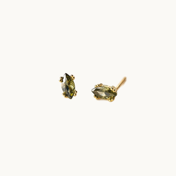 Une paire de boucles d'oreilles est exposée devant un fond beige.  Ce sont des diamants de couleur vert émeraude. La pierre est en forme d'amande, un ovale allongé. Le reste de la boucle d'oreille est en argent 925 plaqué or. 