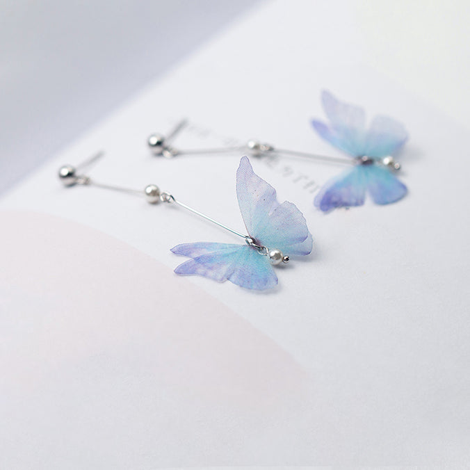 Boucle d'oreille pendante longue avec perle et papillon bleu - Argent 925. Un bijou poétique évoquant le frémissement d'un papillon en plein vol.
