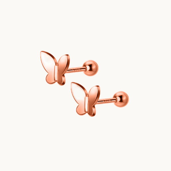 Une paire de boucles d'oreilles est exposée devant un fond beige.  Ce sont des papillons avec une tige droite. Les boucles d'oreille sont en or rose. 