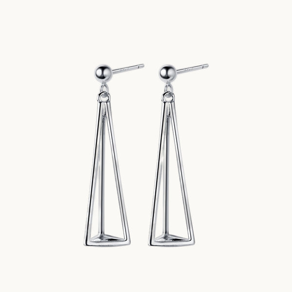 Une paire de boucles d'oreilles est exposée devant un fond beige.  Ce sont des boucles d'oreille pendante en argent. Elles sont en forme de triangles en relief long. 