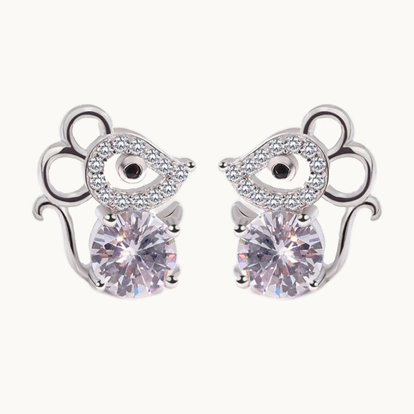 Une paire de boucles d'oreilles est exposée devant un fond beige.  Les boucles d'oreille sont en forme de souris en argent  et en strass