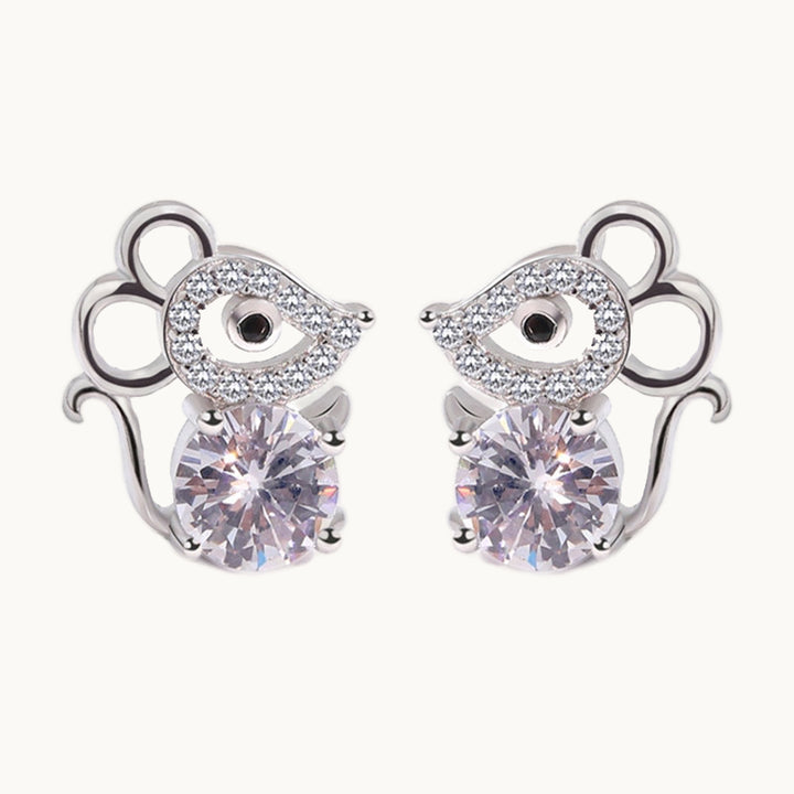 Une paire de boucles d'oreilles est exposée devant un fond beige.  Les boucles d'oreille sont en forme de souris en argent  et en strass