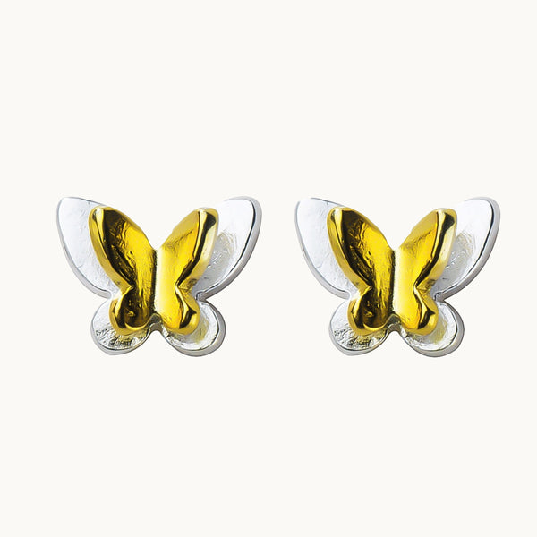 Une paire de boucles d'oreilles est exposée devant un fond beige.  Ce sont des boucles constituées d'un papillon en argent 925 plat surplombé d'un papillon en relief en argent 925 plaqué or.