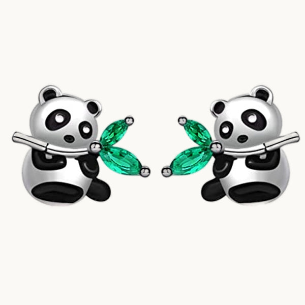 Une paire de boucles d'oreilles est exposée devant un fond beige.  Ce sont des boucles d'oreille en forme de panda. Le panda tient un bambou. Les feuilles sur bambou sont des strass en émeraude vert. 