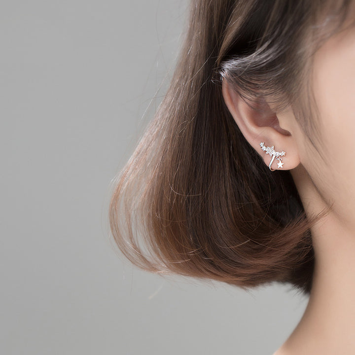 Boucle d'oreille manchette grimpante étoiles strass - Femme - Argent 925. Une vue rapprochée de l'oreille d'une femme avec une boucle d'oreille grimpante en forme d'étoiles scintillantes en strass.