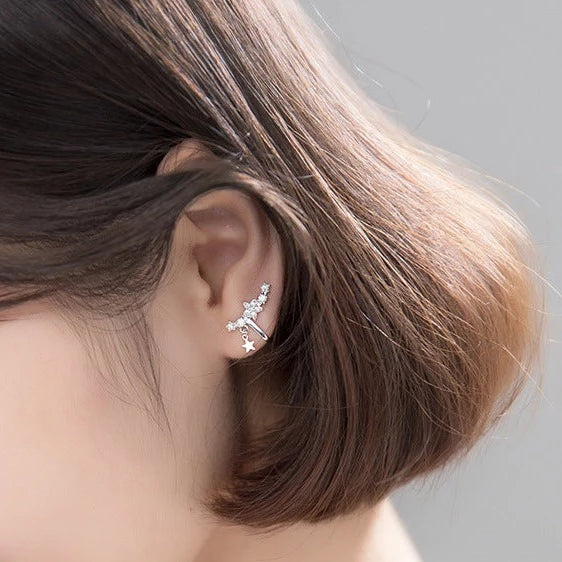 Boucle d'oreille manchette grimpante étoiles strass en argent 925 pour femme. Design unique avec une barre enveloppant délicatement le lobe de l'oreille, étoiles étincelantes en strass montant en cascade, ponctuées par une étoile pendante. Dimensions : 1,6 x 1,2 cm.