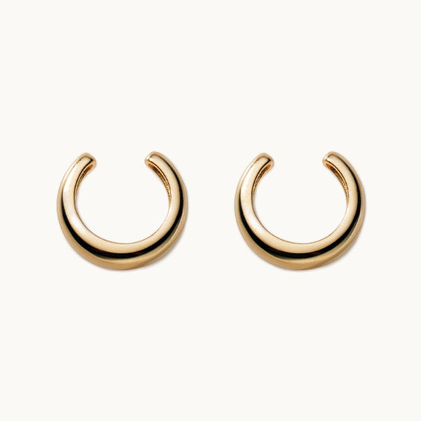 Une paire de boucles d'oreilles est exposée devant un fond beige.  Ce sont des anneaux épais pour cartilage qui ne nécessitent pas de trous. Elles sont en argent 925 plaqué or. 