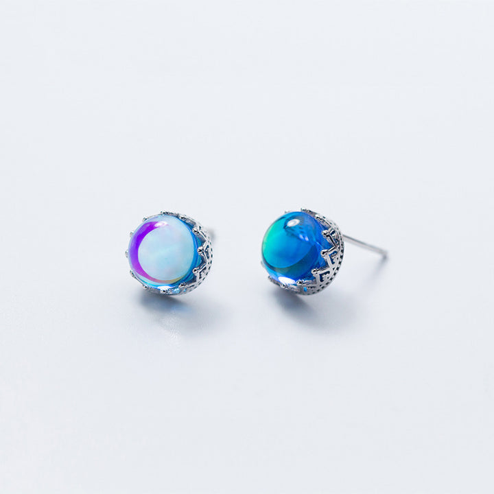 Une paire de boucles d'oreilles en forme de couronne avec un cristal bleu rond irradie des reflets arc-en-ciel. Bijou d'exception en argent 925 pour une allure royale.