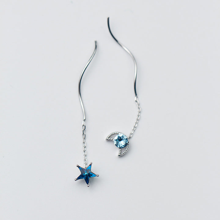 Une paire de boucles d'oreilles pendantes dépareillées en argent 925 avec une étoile et une lune, ornées de diamants de zirconium bleu saphir. Plongez dans le mystère cosmique avec ces bijoux élégants.