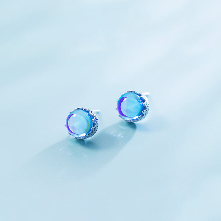 Une paire de boucles d'oreilles en forme de couronne avec un cristal bleu rond irradie des reflets arc-en-ciel, en argent 925. Bijou d'exception pour chaque occasion.