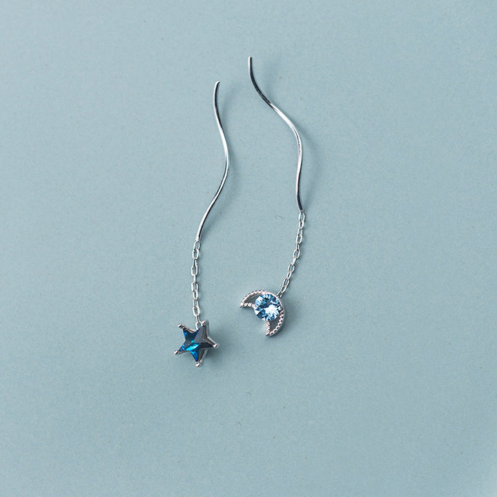 Une paire de boucles d'oreilles pendantes dépareillées avec une étoile et une lune bleues, en argent 925 et ornées de diamants de zirconium. Plongez dans le mystère cosmique avec ces bijoux élégants.