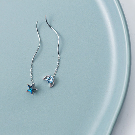 Une paire de boucles d'oreilles pendantes dépareillées en argent 925 avec une lune et une étoile, ornées de diamants de zirconium bleu saphir.